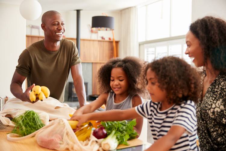 Two parents and two kids unload a bag of produce on a kitchen counter