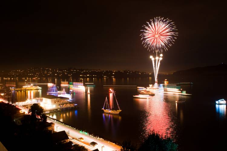 A parade of boats lit up by christmas lights cruise along the shore line 